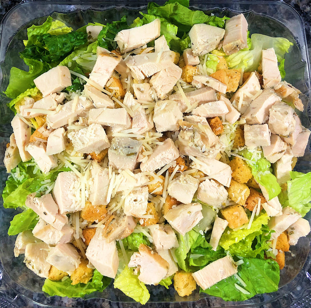 An image of a Chicken Caesar Salad. The salad features fresh, crisp romaine lettuce leaves tossed in a tangy Caesar dressing. It is topped with grilled chicken slices, shaved Parmesan cheese, and crunchy croutons. The salad is garnished with lemon wedges and freshly ground black pepper, creating a visually appealing and mouthwatering combination of textures and flavors.