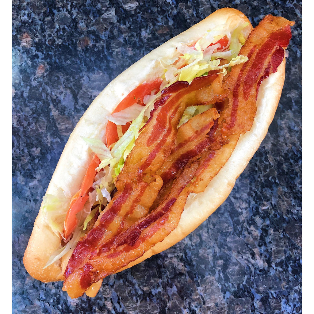 An image of a BLT sub sandwich. The sandwich consists of crispy bacon, fresh lettuce, and sliced tomatoes layered on a toasted sub roll. It is also dressed with mayonnaise and served with a side of pickle spears. The sandwich is neatly arranged and ready to be enjoyed.