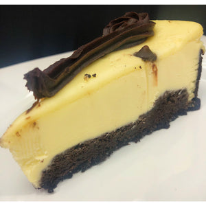 An image of a Black Bottom Cheesecake. The cheesecake has a chocolate cookie crust as the base and a creamy, smooth cheesecake filling. The top layer is rich and chocolatey, with a glossy texture. It is garnished with a dusting of powdered sugar and chocolate shavings. A slice of the cheesecake is served on a dessert plate.